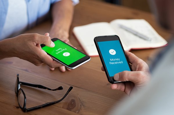 Two people holding cell phones that show money being transferred between them