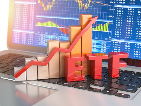 The abbreviation ETF with a bar chart and rising arrow behind it and all sitting on an open laptop with stock charts on the screen.