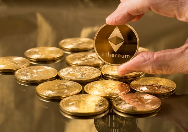 A pile of gold coins and a hand holding up one that says Ethereum.