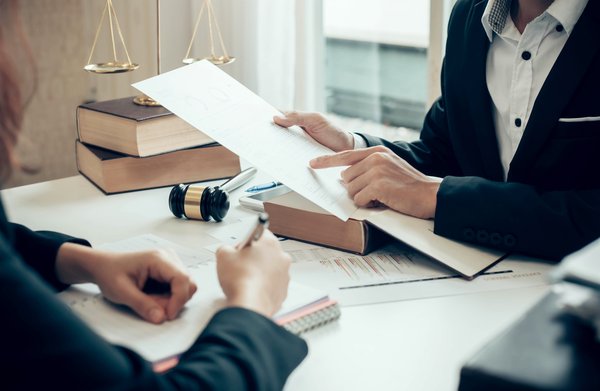 Two people talking and reading paperwork at desk with legal books and gavel.