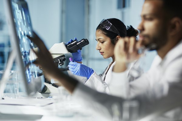 Scientists using a computer and microscope to study life science.