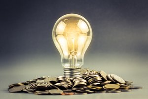 A lit lightbulb with its bottom sitting in a pile of coins.